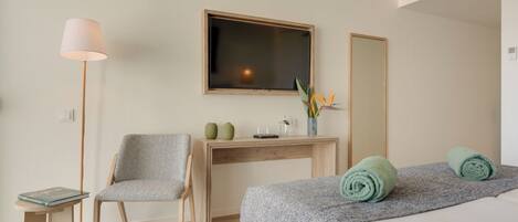A hotel room with a bed, a desk, a chair, a TV, and a mirror.