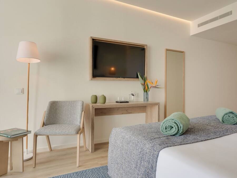 A hotel room with a bed, a desk, a chair, a TV, and a mirror.