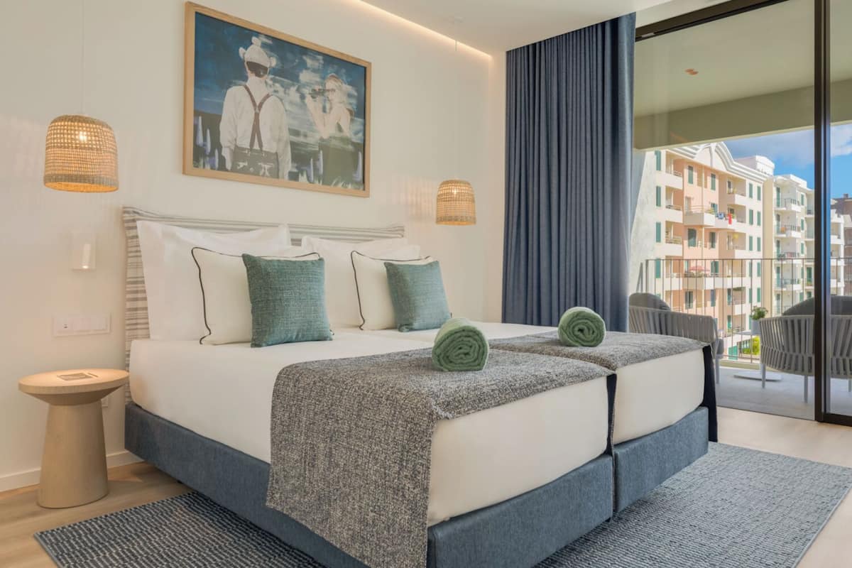 Ein modernes Hotelzimmer mit einem großen Bett, zwei Nachttischlampen, einem Gemälde und einem Balkon mit Stadtblick.