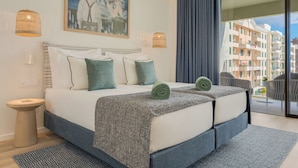 A modern hotel room with a large bed, two bedside lamps, a painting, and a balcony with a view of the city.