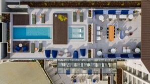 A rooftop pool area with multiple seating areas, a central pool, and a glass-enclosed section.