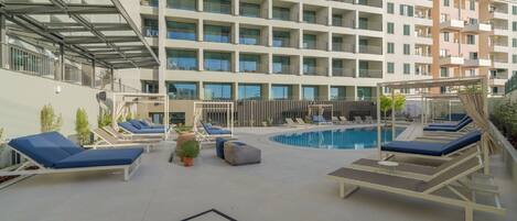 A rooftop pool area with sun loungers and a swimming pool, surrounded by a multi-story building with balconies.