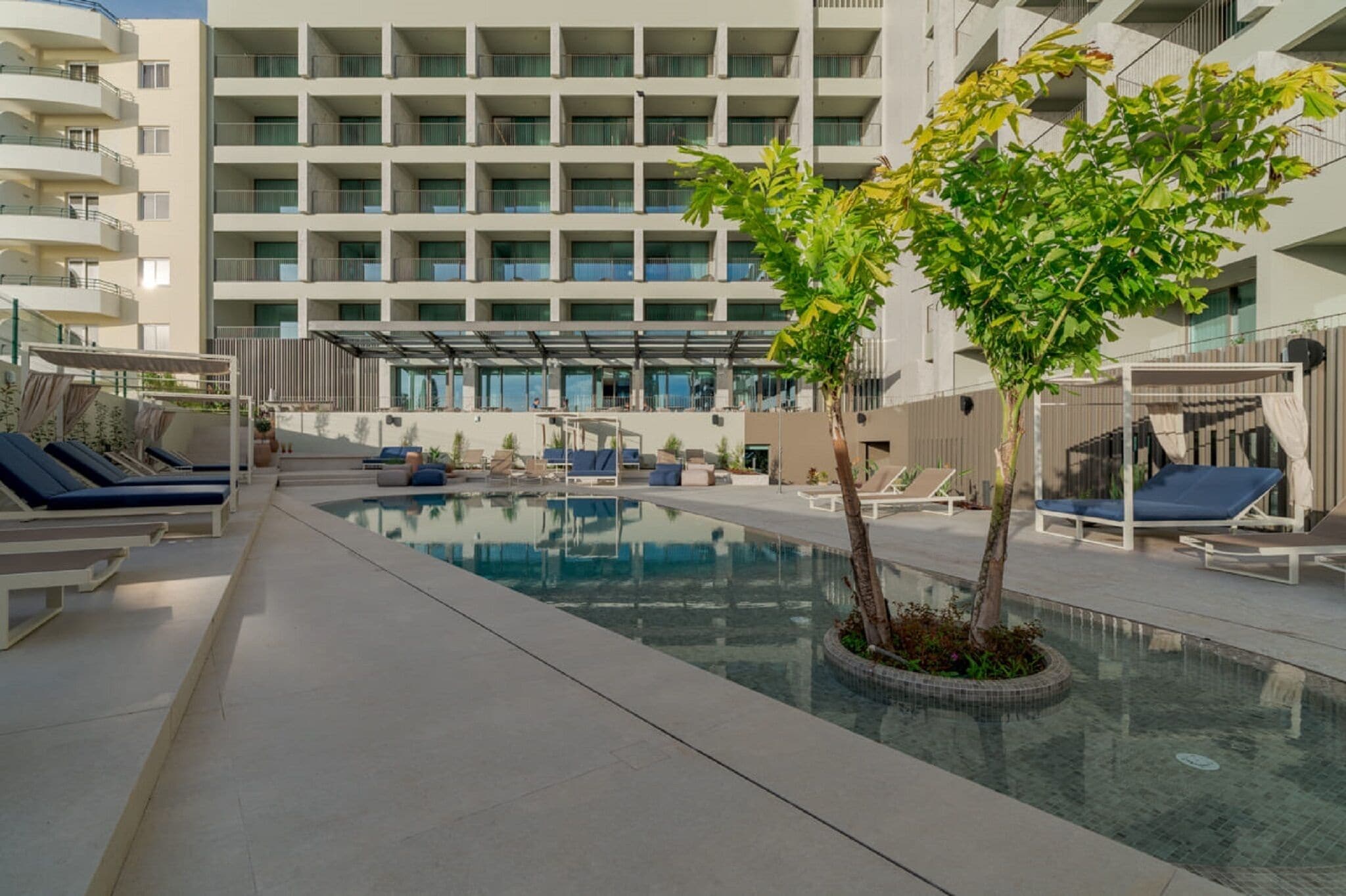 A modern hotel pool area with multiple lounge chairs and a central pool.