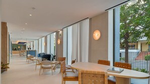 A modern dining area with a round table, wooden chairs, and large windows offering a view of the street.