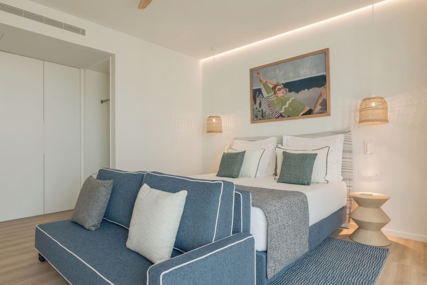 Een moderne slaapkamer met een bed, een blauwe bank en een schilderij aan de muur.