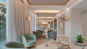A modern hotel lobby with seating areas, a bar, and a large window with curtains.