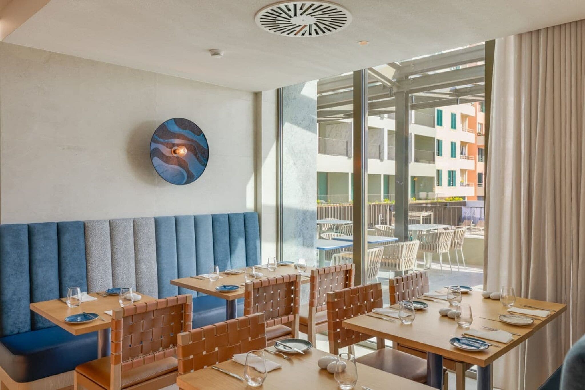 A modern restaurant with high tables and booths, large windows offering a view of the city, and a unique wall art piece.