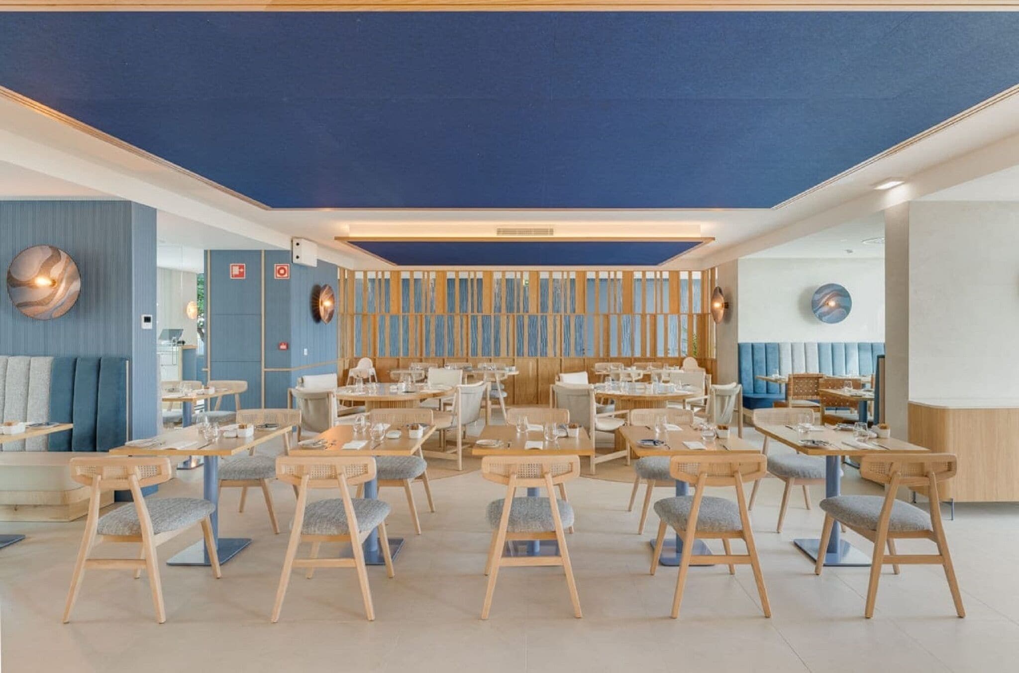 En moderne restaurant med træborde og stole, blå vægge og dekorative væglamper.