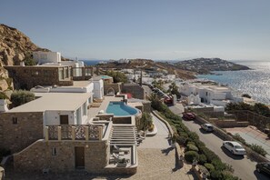 A coastal town with stone buildings, a swimming pool, and a road with parked cars. - Spacious 6-bedroom house with WiFi and AC in lovely Mykonos (Mykonos)