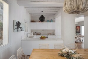 A modern kitchen with white cabinetry, a wooden dining table, and wicker chairs. - Spacious 6-bedroom house with WiFi and AC in lovely Mykonos (Mykonos)