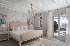 A bedroom with a marble wall, a bed with a headboard, a chandelier, a nightstand, and a view through a glass door. - Spacious 6-bedroom house with WiFi and AC in lovely Mykonos (Mykonos)