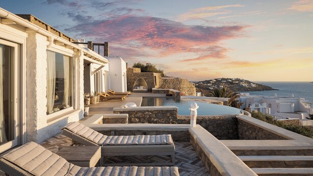 Terraço no telhado com cadeiras de lounge, piscina e vista para o mar e edifícios ao longe.