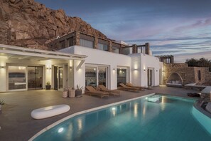 A modern villa with a swimming pool, outdoor seating, and a view of rocky terrain. - Spacious 6-bedroom house with WiFi and AC in lovely Mykonos (Mykonos)