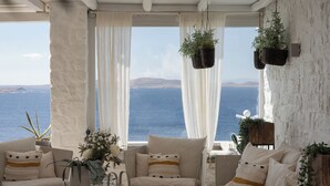 Quarto aconchegante com vista para o mar, com sofá, poltrona e plantas penduradas.