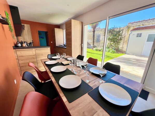 A modern dining area with a long table set for six, equipped with plates, glasses, and black placemats.