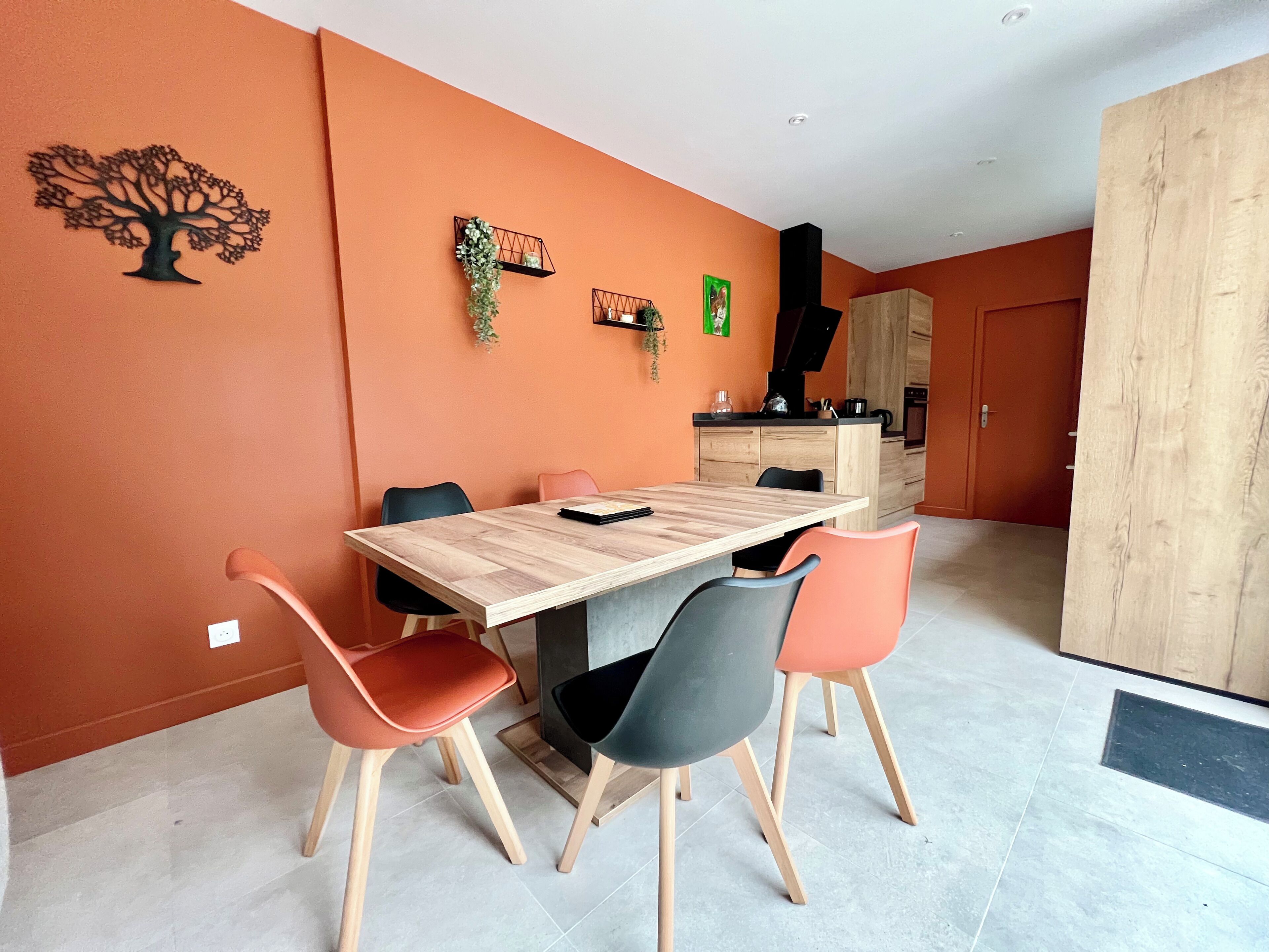 Un espace repas moderne avec une table et des chaises en bois, une cuisine en arrière-plan et une grande armoire.