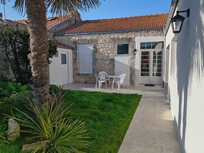 A stone building with a tiled roof, a small patio with white chairs, and a well-maintained lawn. - Large house 10 minutes from the town centre - Nice garden and petanque area (La Rochelle)