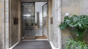 Une entrée d’immeuble avec un portail en métal, un escalier et une grande plante en pot.