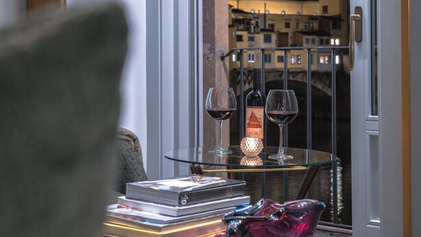 Un balcon avec une table en verre sur laquelle sont posés des verres à vin et une bouteille, une chaise et une pile de livres.