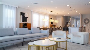 A modern living room with a grey sofa, two round gold tables, and a white armchair.