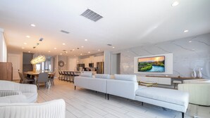 A modern living room with a sofa, dining area, kitchen, and a TV mounted on the wall.