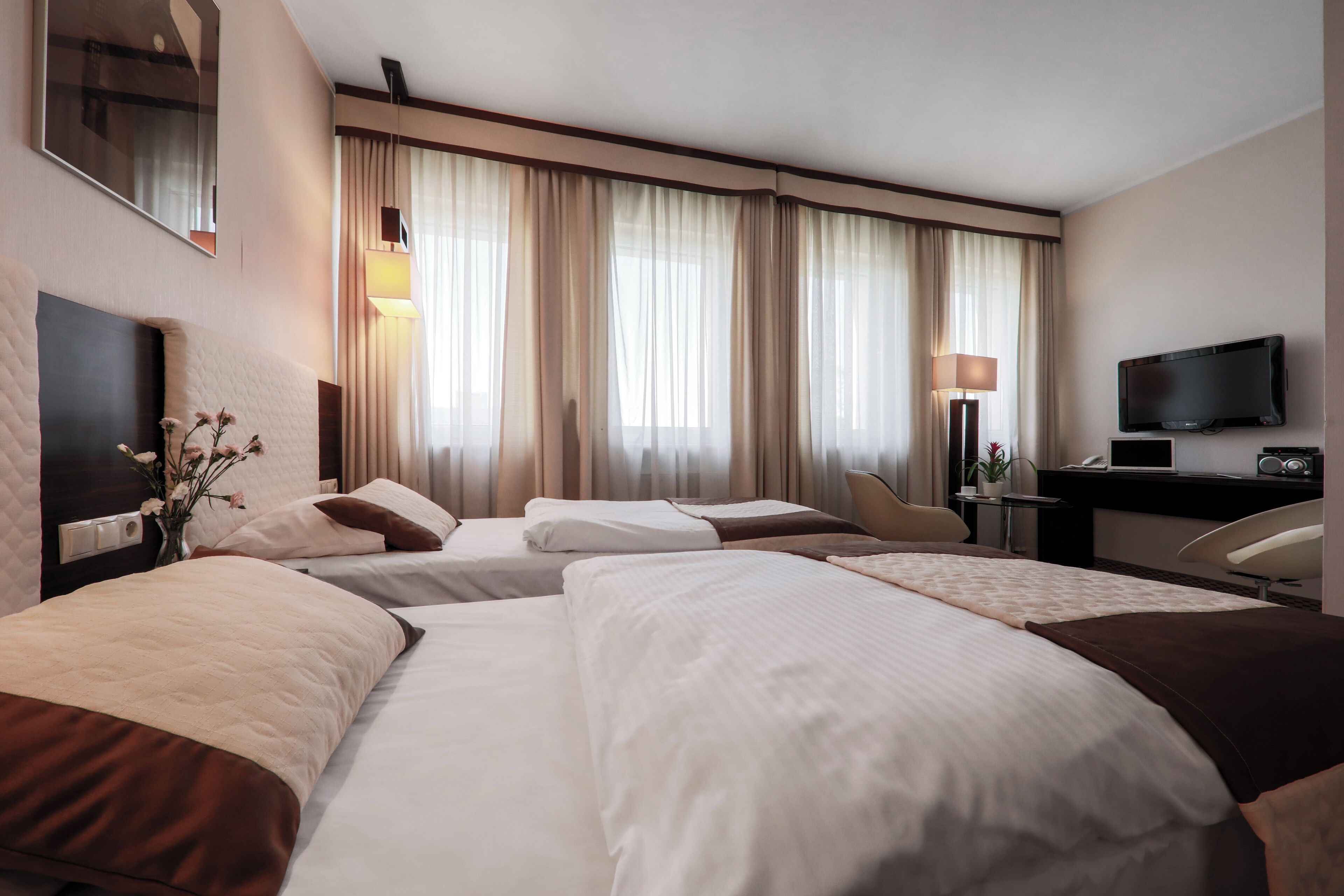 Habitación de hotel con dos camas, un escritorio, un televisor y un amplio ventanal con cortinas.