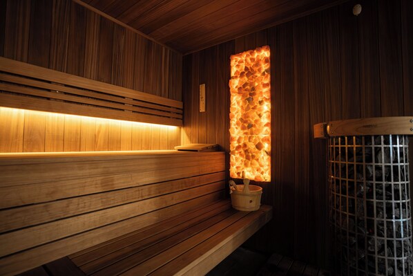 A wooden sauna with benches and a stone wall emitting light. - Hotel Borowiecki (Lódz)