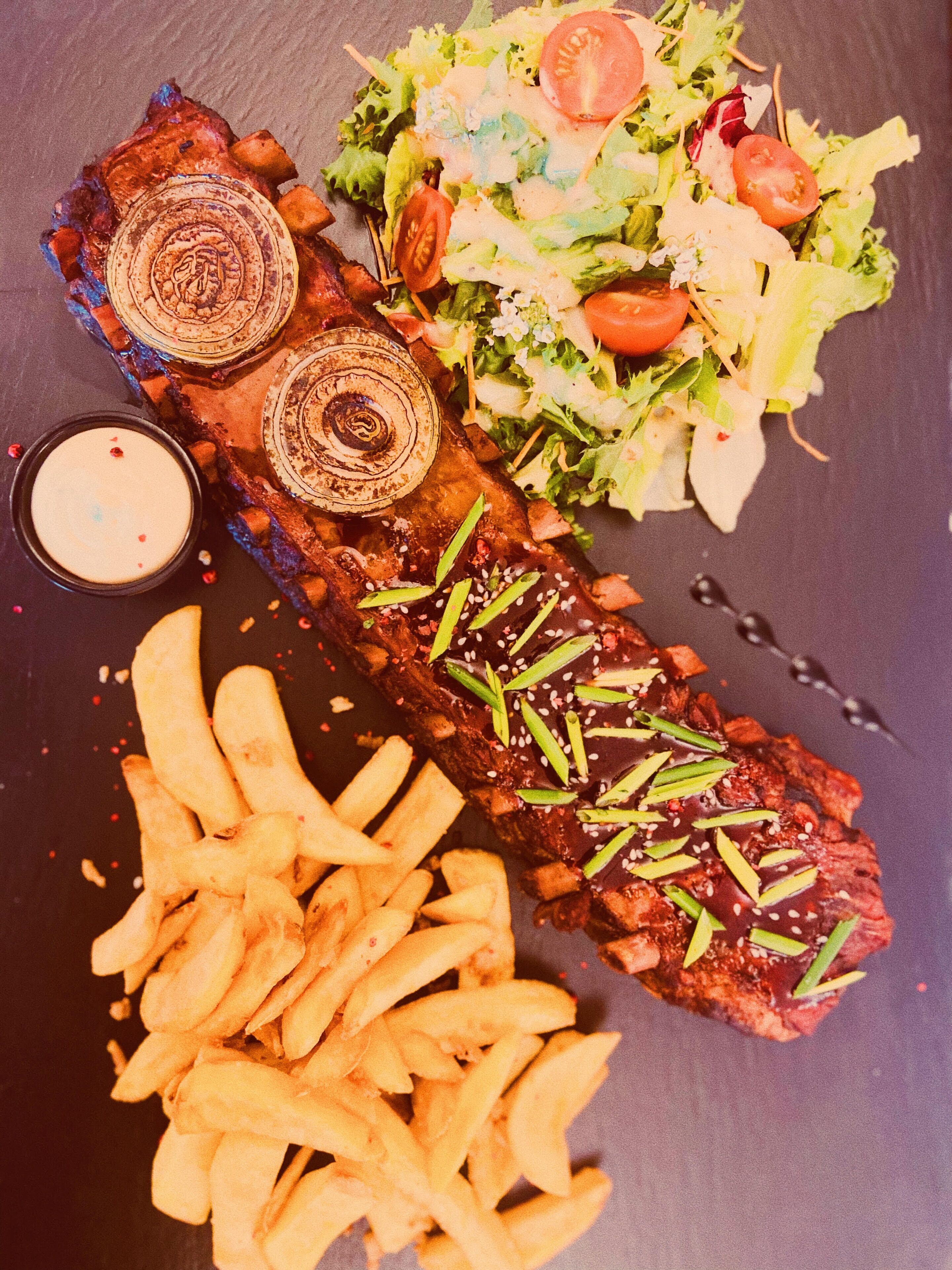 Een steak met een decoratieve garnering, vergezeld van een salade en frieten.
