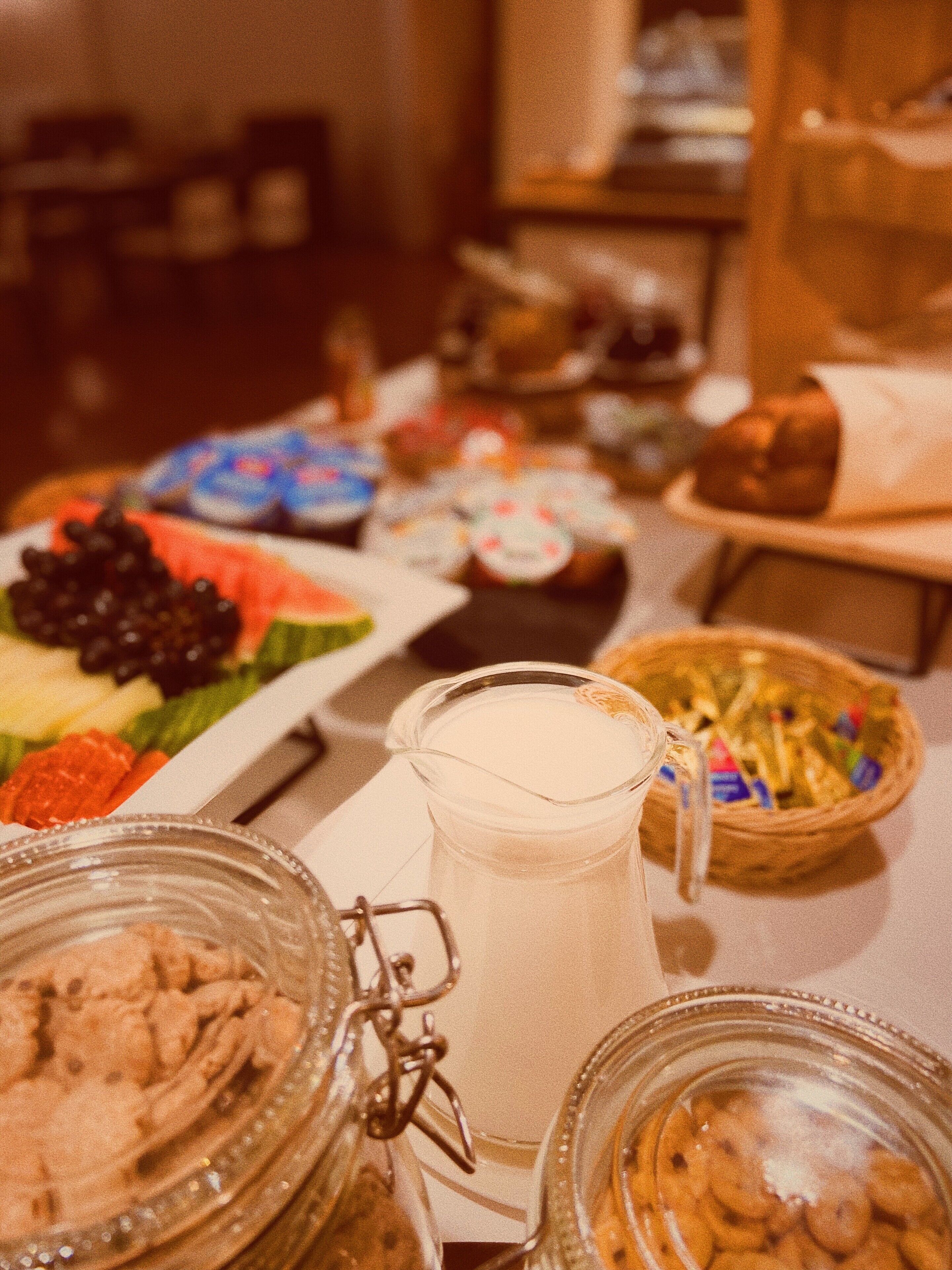 Una mesa con diversos alimentos, como una jarra de leche, un plato de frutas y varios recipientes con aperitivos.