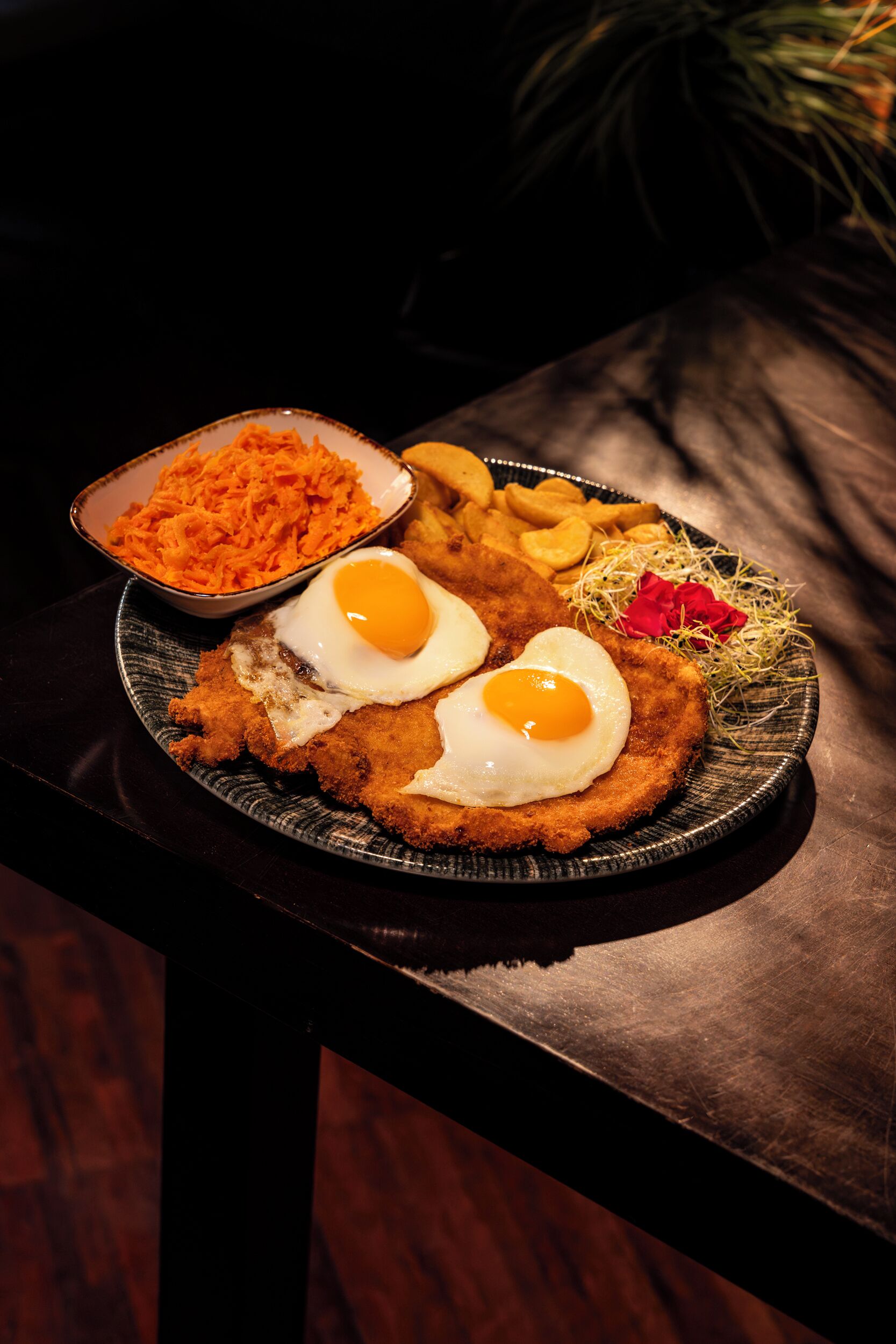 Une assiette composée d’une escalope panée, d’œufs au plat, de frites et de carottes râpées.