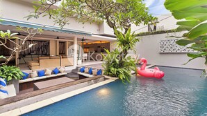 A pool area with a lounge, a tree, and a pink flamingo float.
