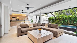 A modern living room with a sectional sofa, a wooden coffee table, and a view of a kitchen and outdoor area.