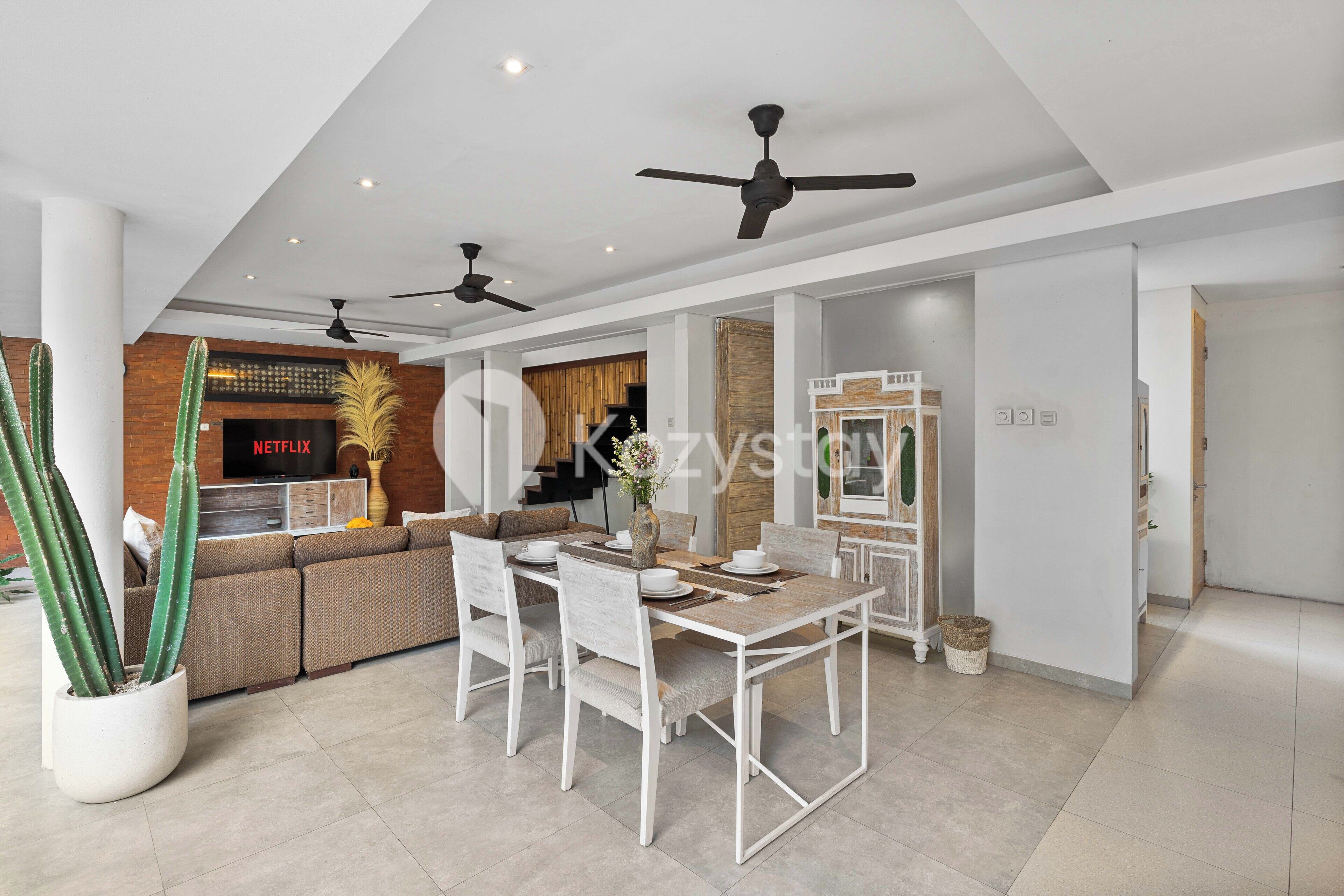 A modern living room with a dining area, featuring a sofa set, a dining table, and ceiling fans.