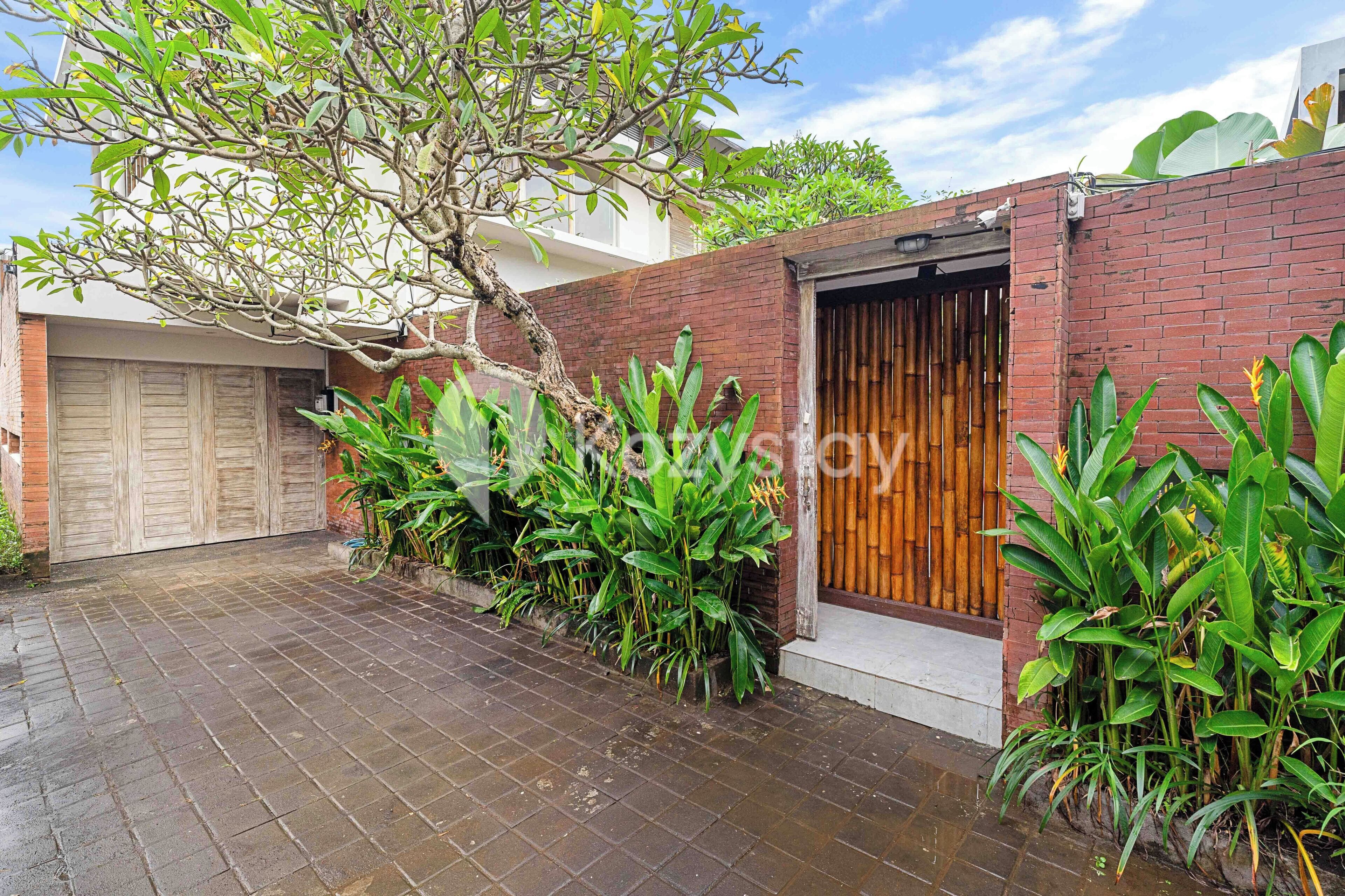 Um imóvel residencial com muro de tijolos, porta de madeira e acesso por calçada de ladrilho.
