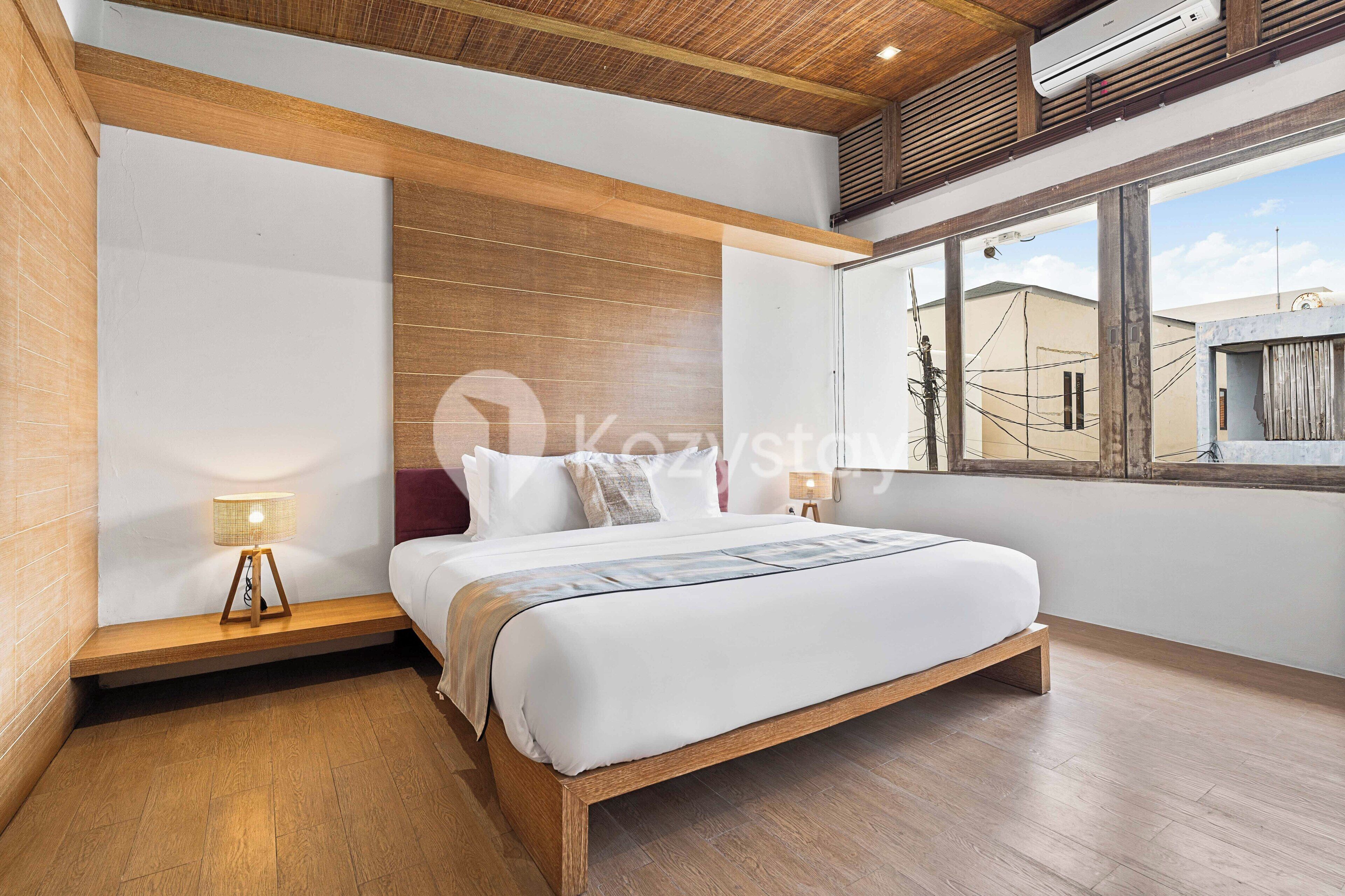 Un dormitorio moderno con estructura de cama de madera, una lámpara de noche y vistas al exterior a través de un ventanal amplio.