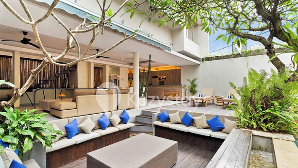 A modern outdoor living area with multiple seating options, including sofas and a coffee table, surrounded by plants and a wooden deck.