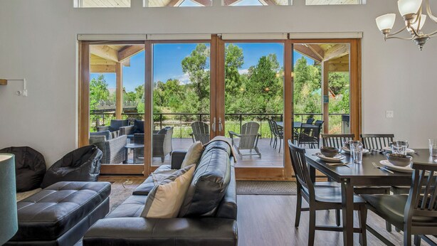 Amplia sala de estar con un gran ventanal corredizo que da a una terraza exterior, amoblada con un sofá, sillas y una mesa de comedor para cuatro.