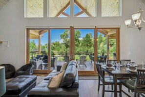 Un vaste espace de vie avec une grande porte-fenêtre coulissante donnant sur une terrasse extérieure, aménagée avec un canapé, des fauteuils et une table à manger pour quatre personnes.