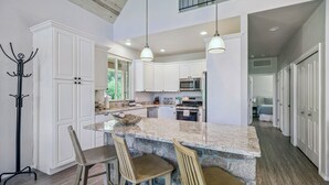 Una cocina amplia con armarios blancos, encimera de granito y una isla central con taburetes de bar.
