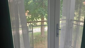 A view through a screened door with a metal gate, leading to an outdoor area with a tree and a fence. - 5 Guests - Pet Friendly - Balcony & Free Parking (Dartford)