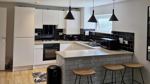 A modern kitchen with white cabinets, a black stove, and a large island with stools. - 5 Guests - Pet Friendly - Balcony & Free Parking (Dartford)