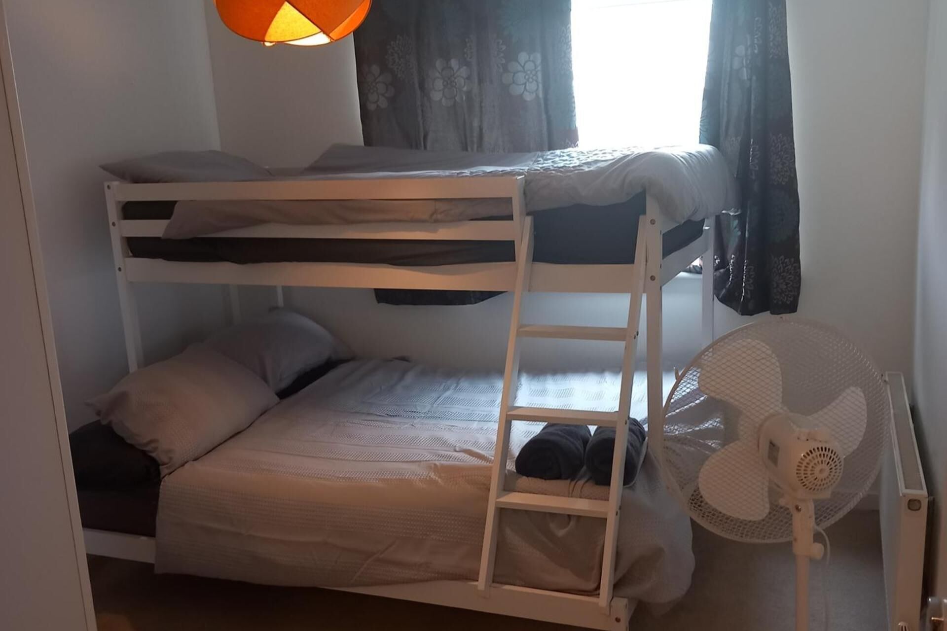 Une chambre avec un lit superposé, un ventilateur blanc et des rideaux.