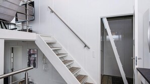 Un intérieur moderne avec un escalier menant à un deuxième étage, une porte dotée d’un panneau en verre et une petite table sur laquelle sont posés divers objets.