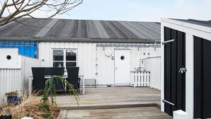Un bâtiment doté d’une terrasse en bois, d’une clôture blanche et d’une porte noire.