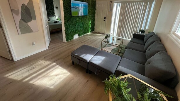 Una sala de estar moderna con un sofá modular gris, una mesa de centro de vidrio y una pared verde con un televisor.