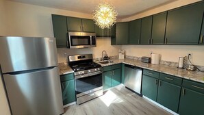 Una cocina moderna con electrodomésticos de acero inoxidable, armarios verdes y una encimera de mármol.