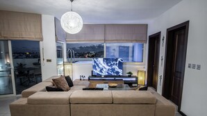 A modern living room with a large flat-screen TV, a beige sofa, and a glass coffee table. - D Pool Top (L-Imsida)
