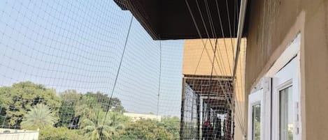A balcony with a net, a door, and a view of trees and a building in the background.
