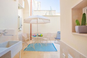 A small patio area with a table, chairs, a white umbrella, and a potted cactus.