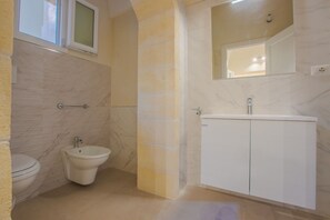 Een badkamer met toilet, bidet en wastafel met spiegel erboven.